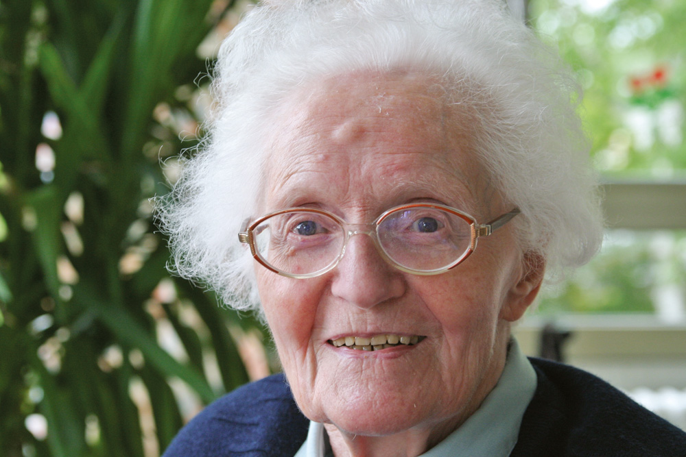 Lächelnde 90-jährige Dame mit Brille und grauen lockigen Haaren
